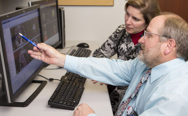 Care providers sit at a computer and look at CT scan results on a monitor.