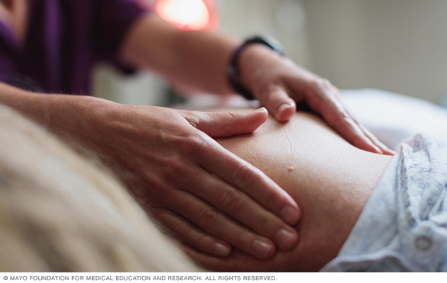 A massage therapist works on the shoulder of someone in a hospital gown.