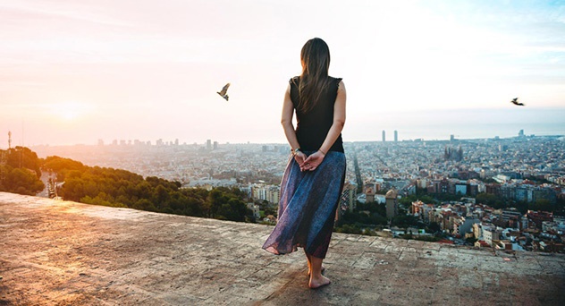 A barefoot woman stands at an overlook above Barcelona, Spain.