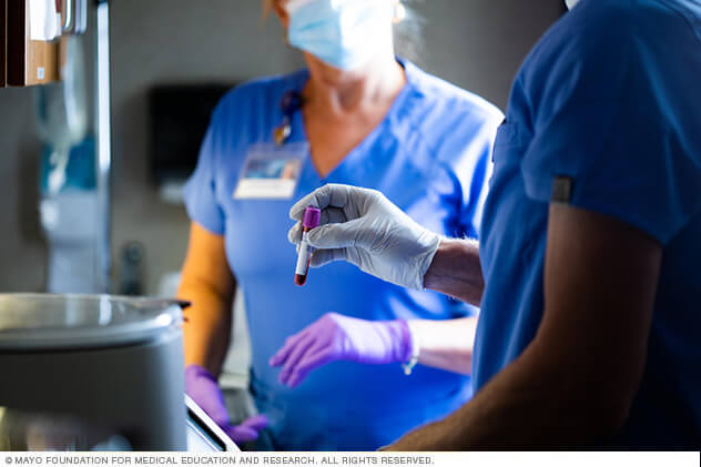 A technician's gloved hand holds a whole blood sample in a blood collection tube.