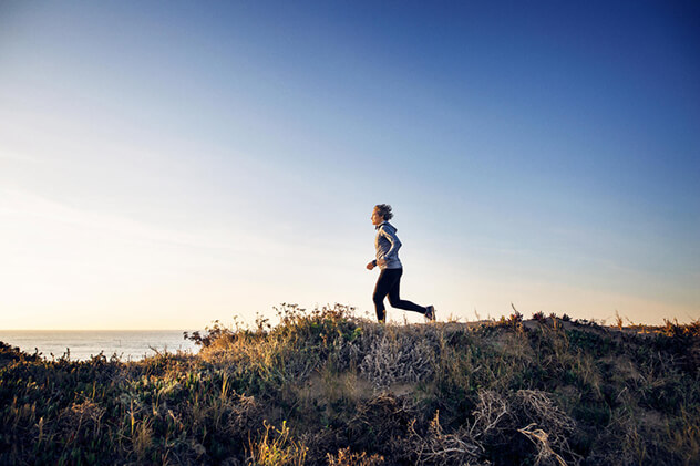 A woman jogs across beach dunes.