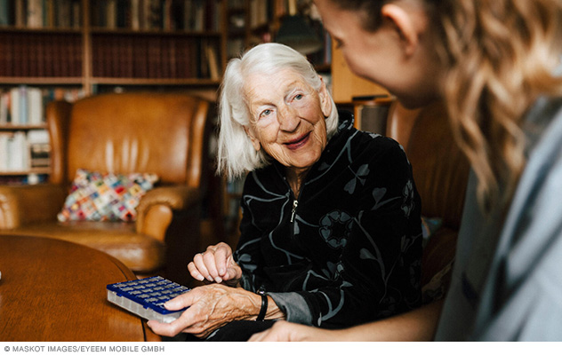 A person holds a box of organized medicines and talks with a home care nurse.