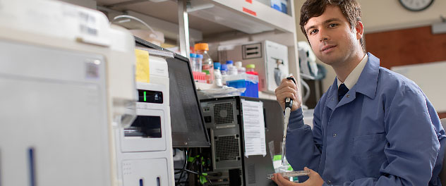 An investigator with a pipette and petri dish stands beside lab equipment.