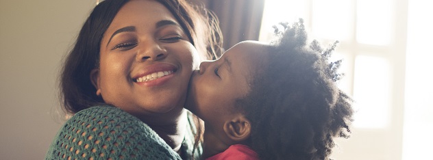 Little girl kissing smiling woman on the cheek