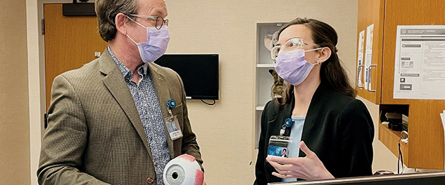 Clinician-scientists in conversation; one holds an anatomical model of an eye