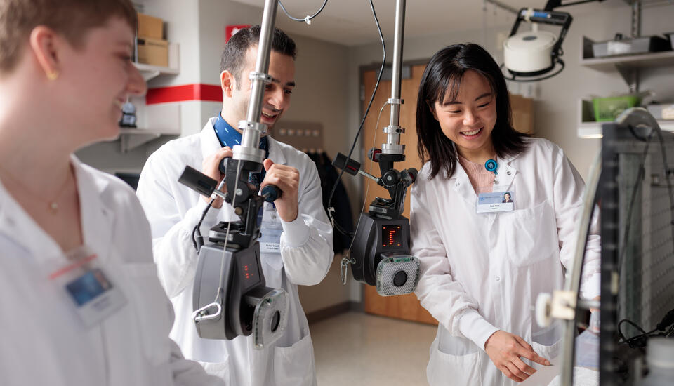 Photograph of three lab workers standing together wearing white lab coats and discussing research