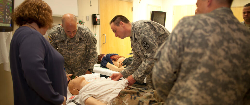 Service members in camouflage using medical simulation device