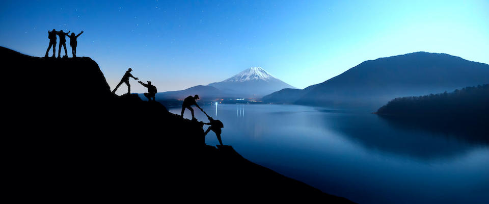 Silhouettes of hikers reaching a high point